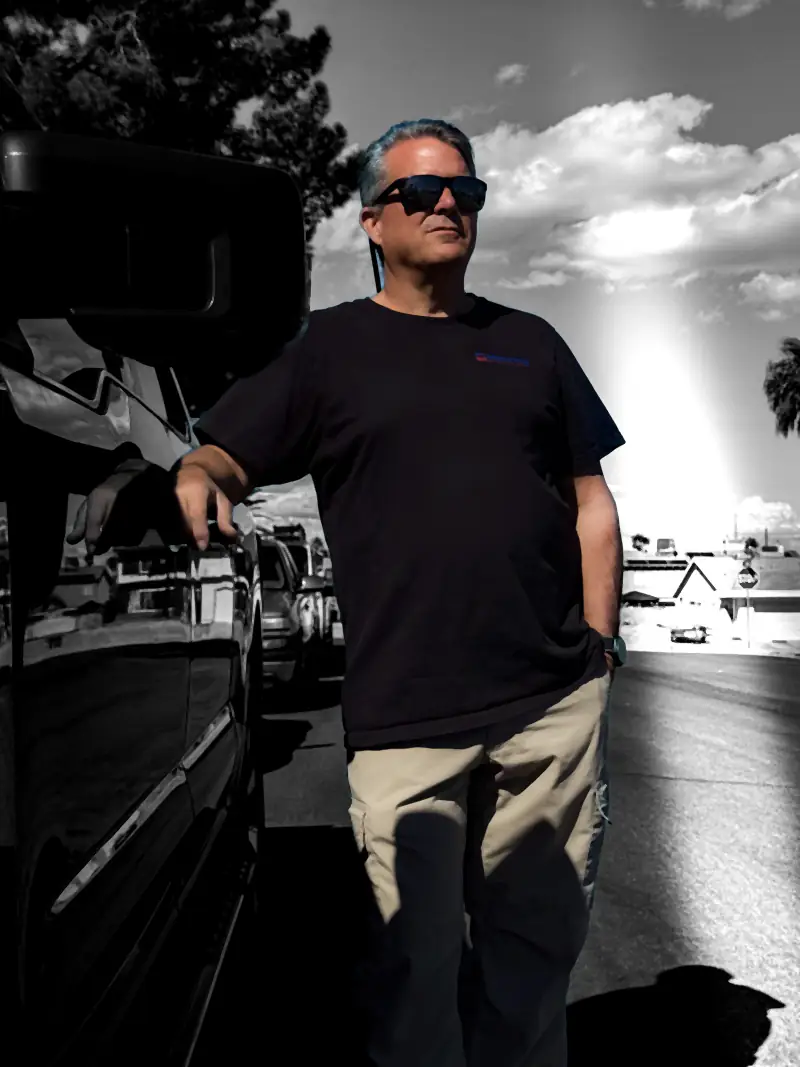Black-and-white portrait of the founder of Manring Heating & Air in a branded shirt and sunglasses beside a vehicle