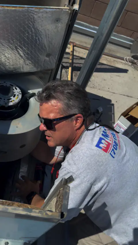 Technician in a Manring Heating & Air shirt servicing an air conditioning unit on a roof